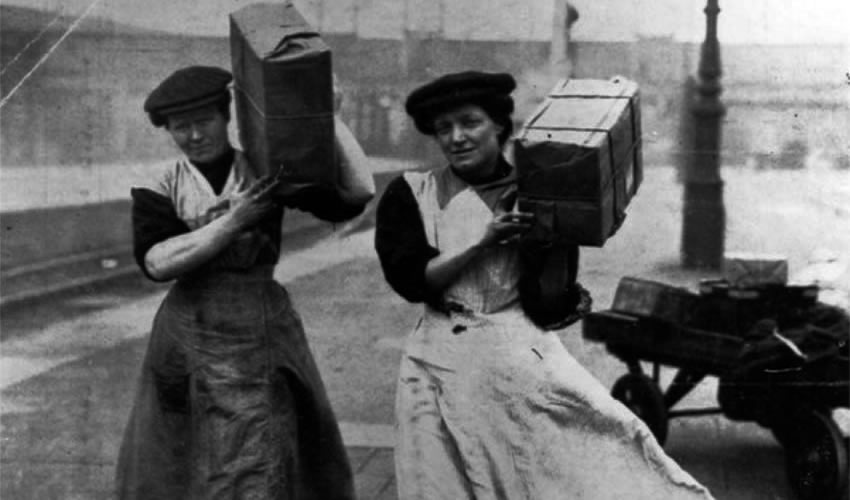 Dos mujeres británicas cargan paquetes, mientras trabajan como porteras, en Londres, fotografía publicada originalmente en 1915 por The Illustrated London News)